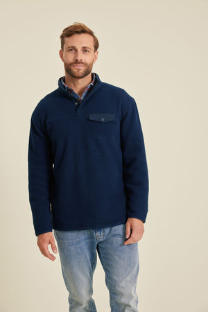 Man wearing a navy fleece pullover and light blue jeans on a beige background