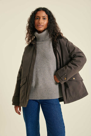 Woman wearing a brown jacket over a gray sweater and blue jeans on a beige background
