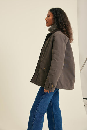 Woman wearing a brown jacket and blue jeans against a plain background