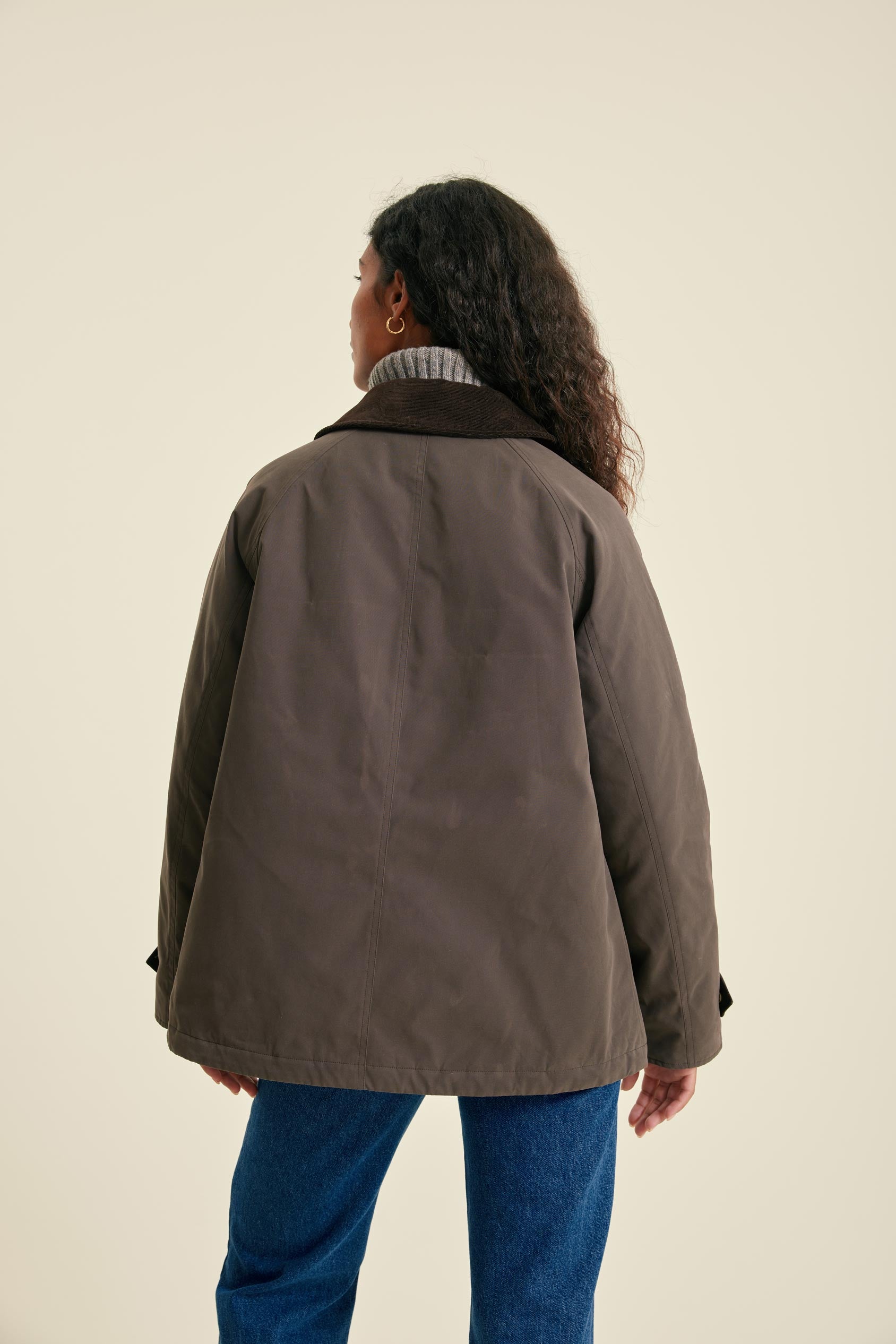 Person wearing a brown jacket and blue jeans on a beige background