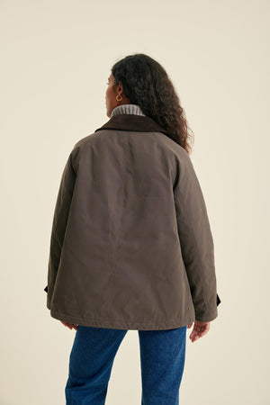 Person wearing a brown jacket and blue jeans on a beige background