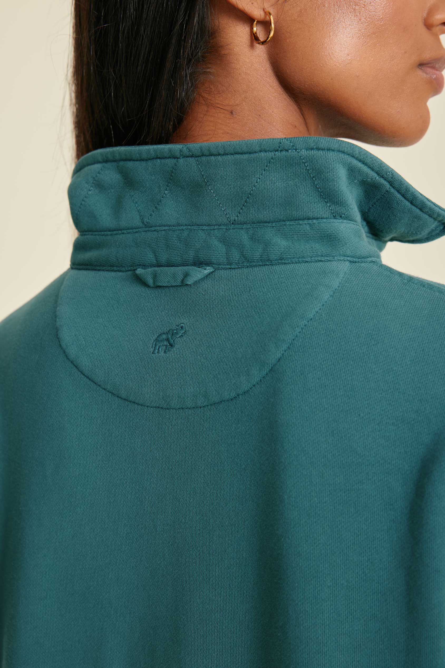Close-up of a pine sweatshirt with a brand logo on the collar against a neutral background