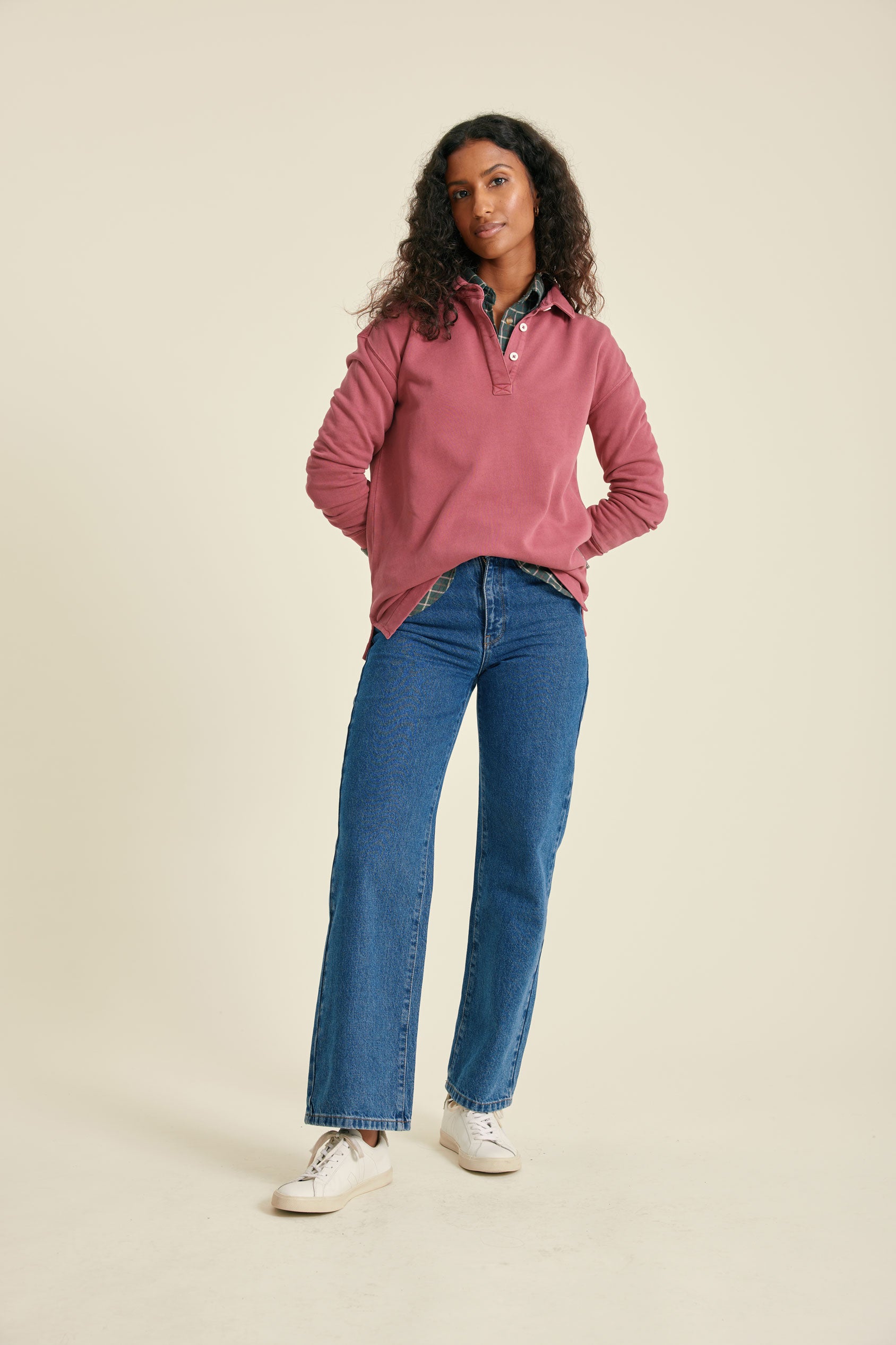Woman wearing a pink sweat and blue jeans on a beige background