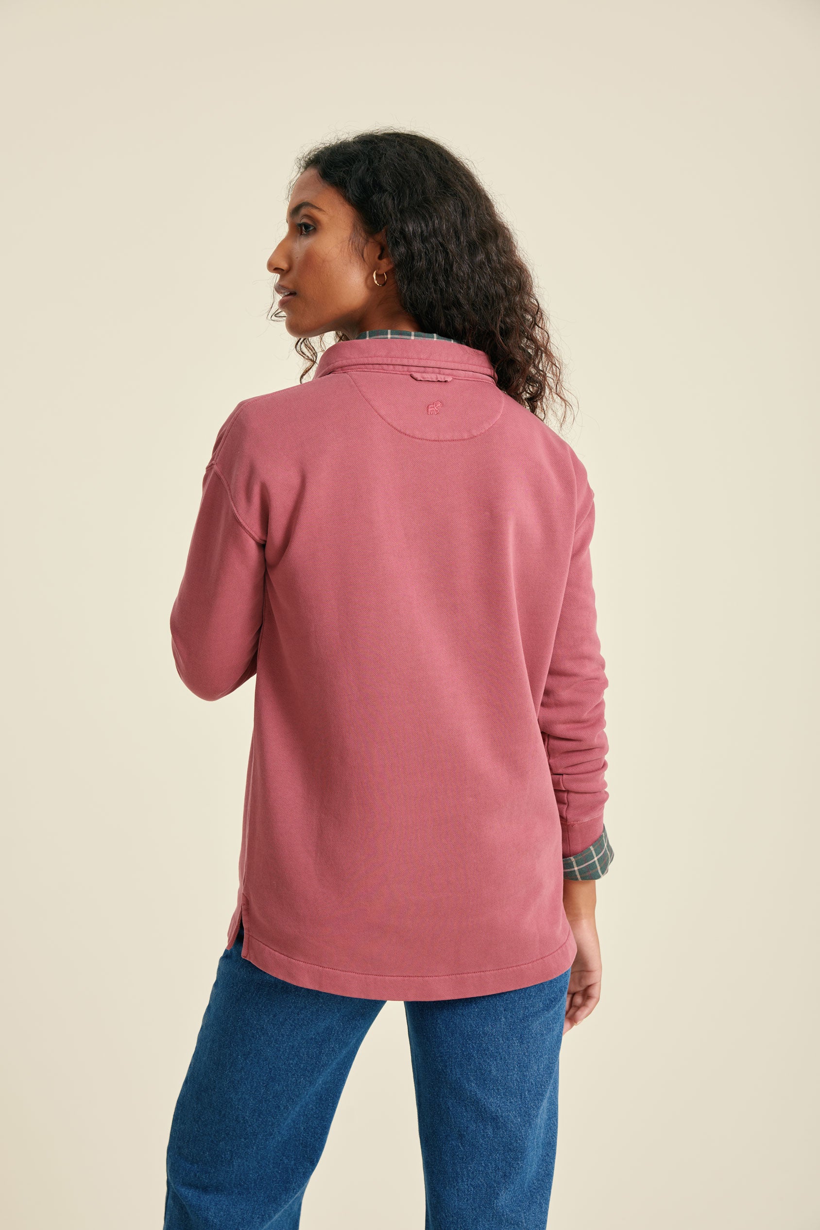 Woman wearing a pink sweatshirt and blue jeans against a beige background