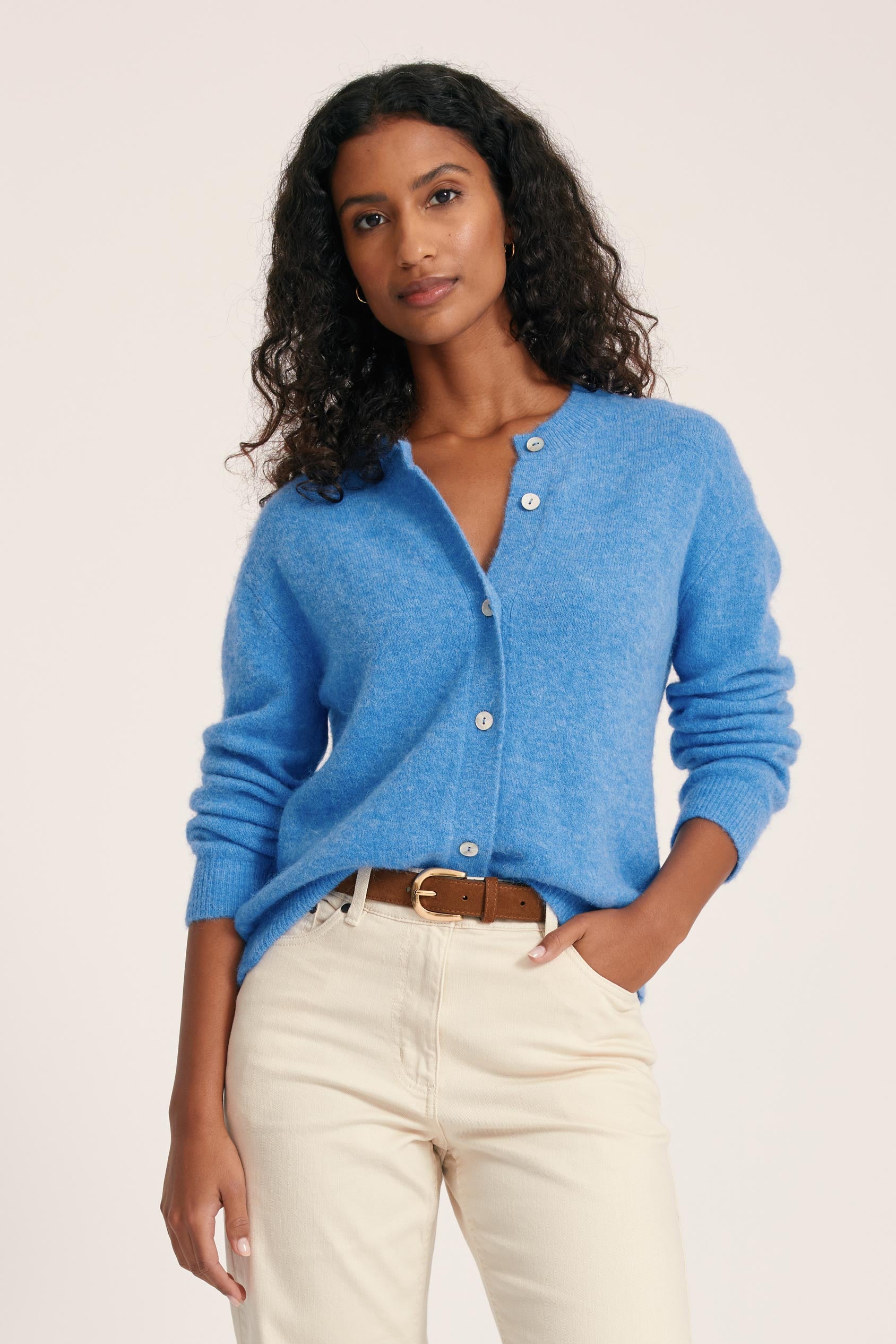 Woman wearing a blue cardigan and beige pants on a plain background