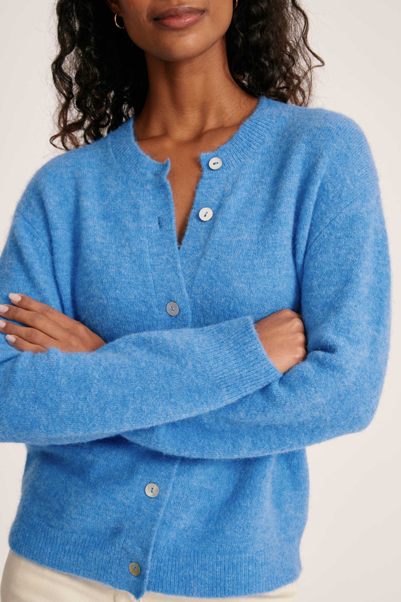 Woman wearing a blue cardigan with button details on a white background