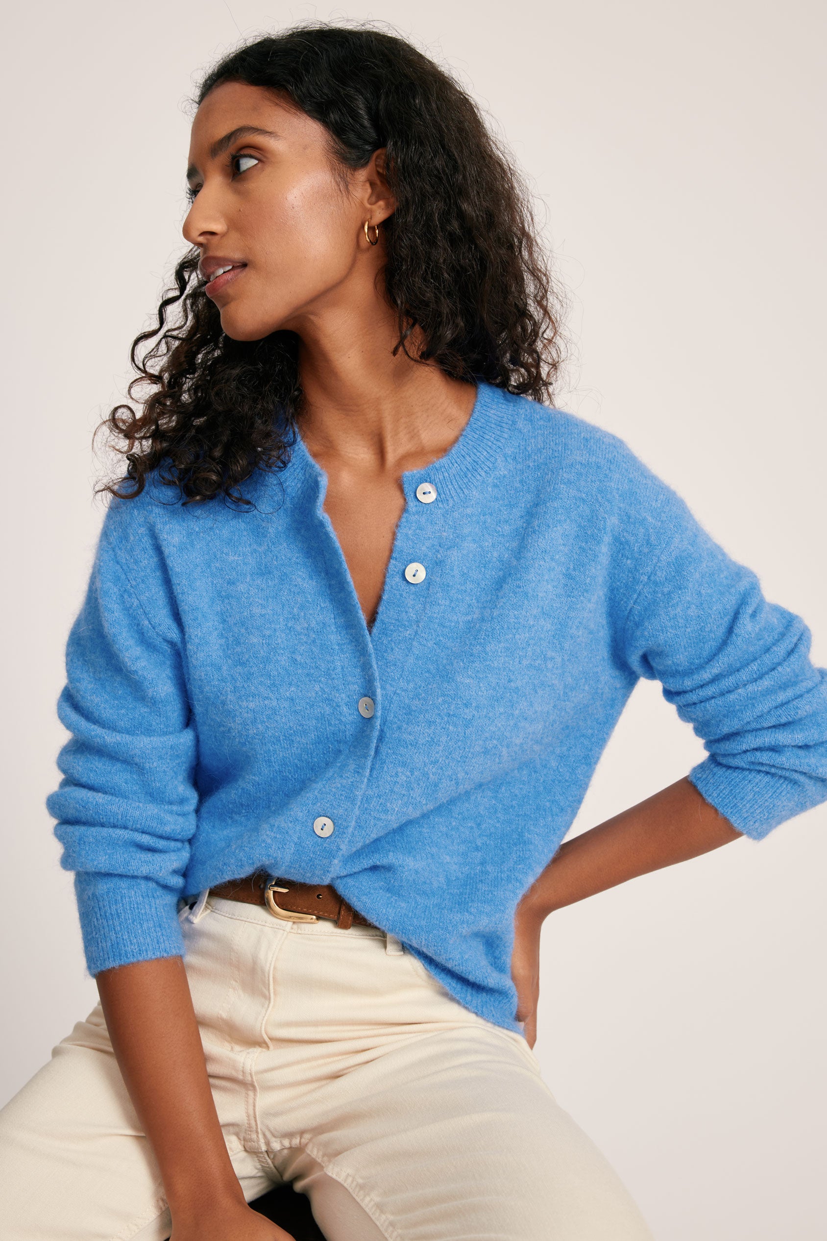 Woman wearing a blue cardigan sitting on a white surface