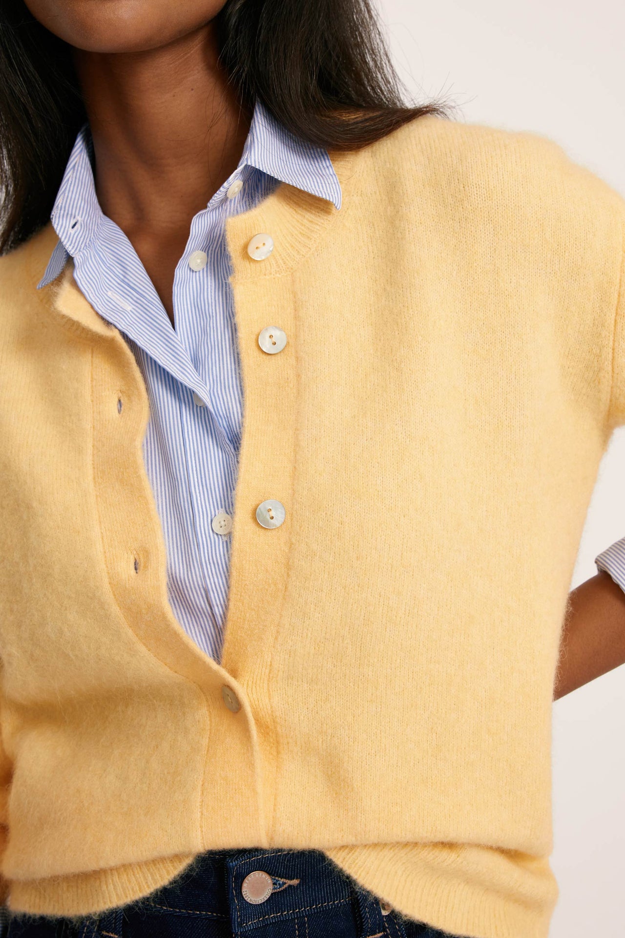 Yellow cardigan over a blue shirt with a white background