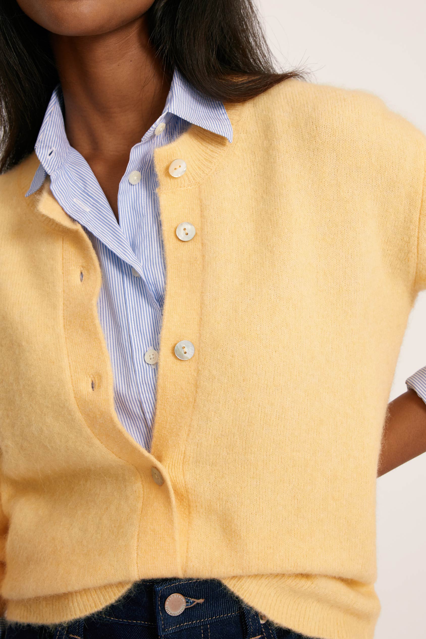 Yellow cardigan over a blue shirt with a white background