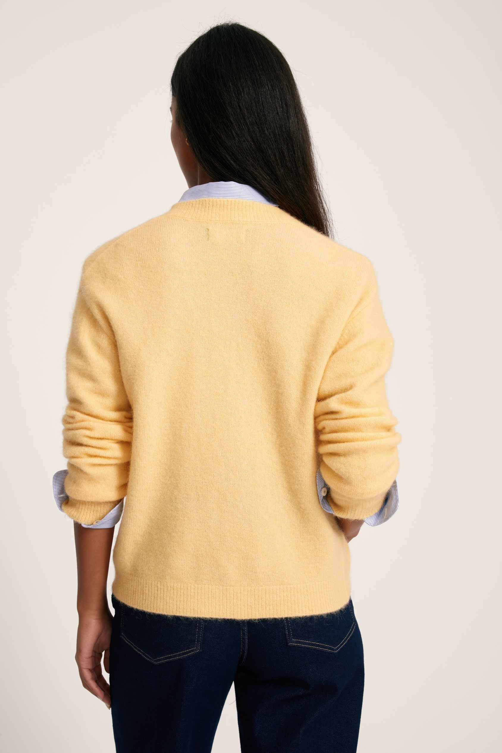 Person wearing a yellow sweater with rolled-up sleeves on a plain background