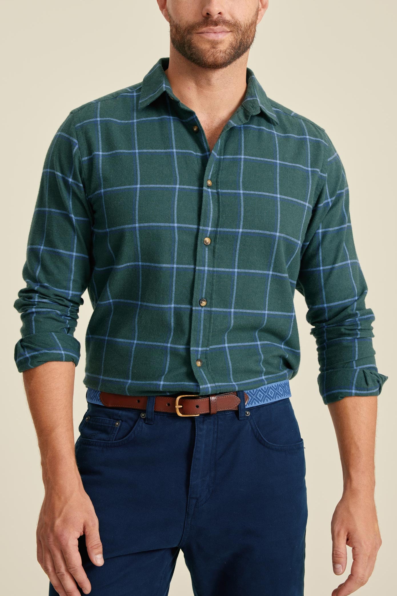 Man wearing a green plaid shirt and blue pants on a beige background
