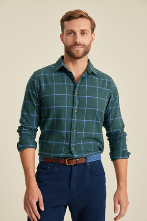 Man wearing a green plaid shirt and blue pants on a beige background
