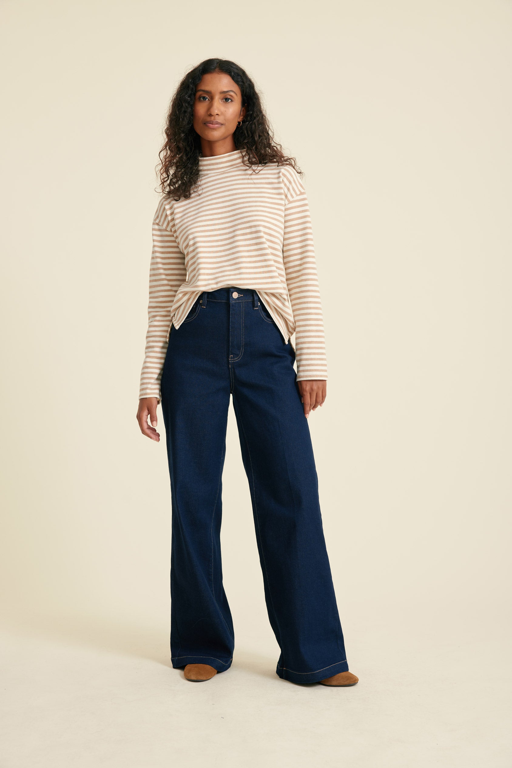 Woman wearing a striped top and blue jeans on a beige background