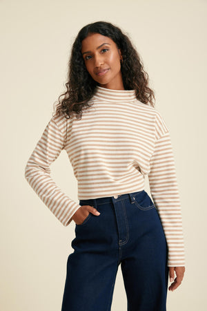 Woman wearing a striped top and blue jeans against a beige background