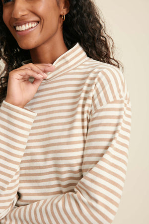 Woman wearing a beige and white striped long-sleeve top against a neutral background