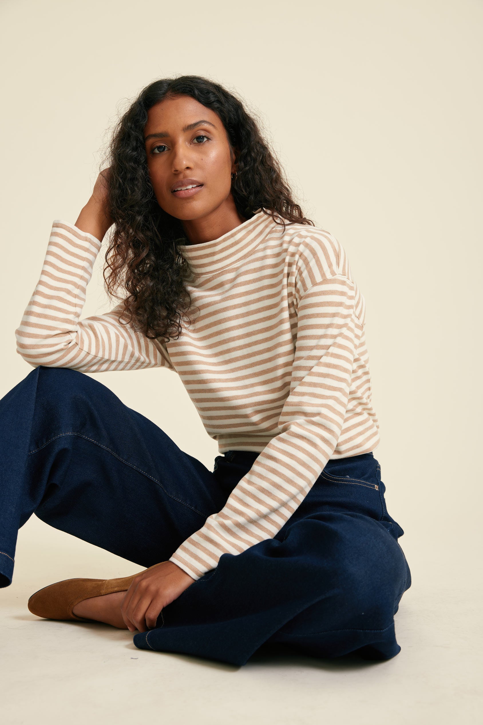 Woman wearing a striped tee and blue pants sitting on a white background