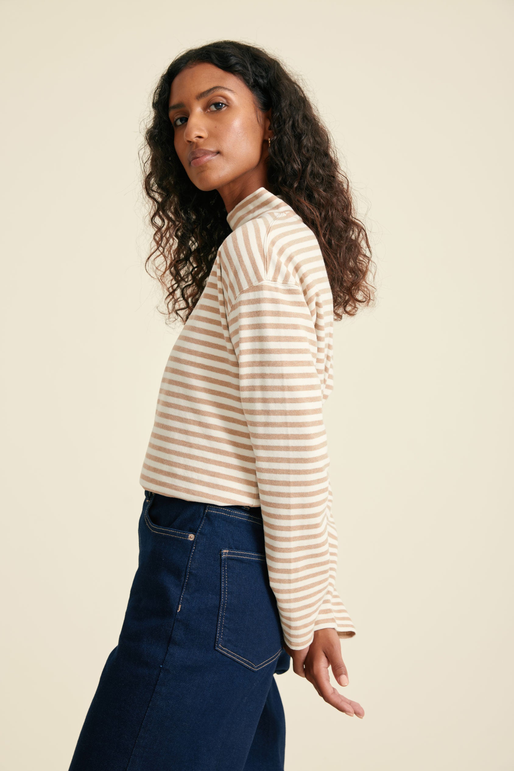 Woman wearing a striped top and blue jeans against a beige background