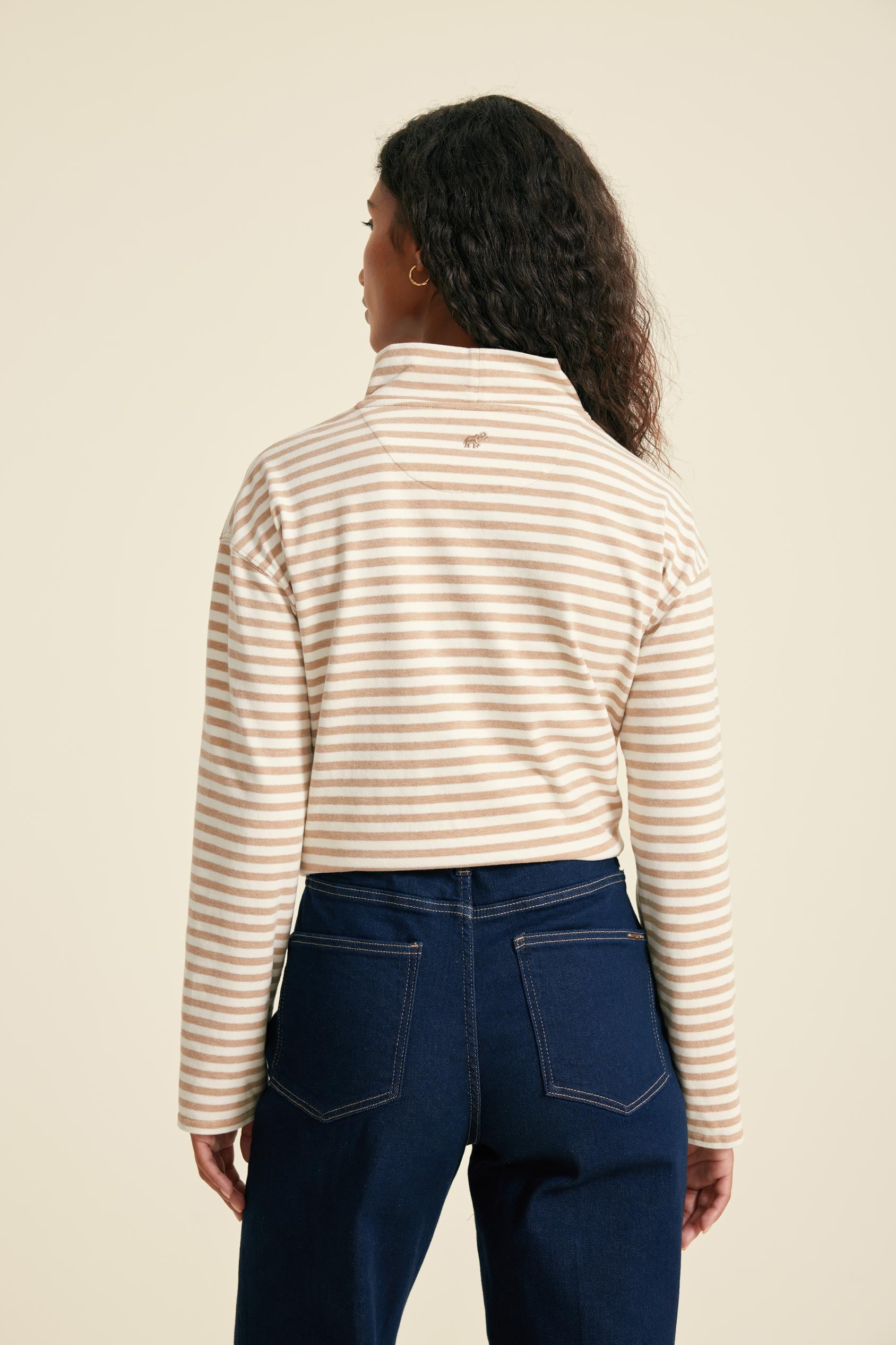 Person wearing a striped long-sleeve top and blue jeans on a beige background