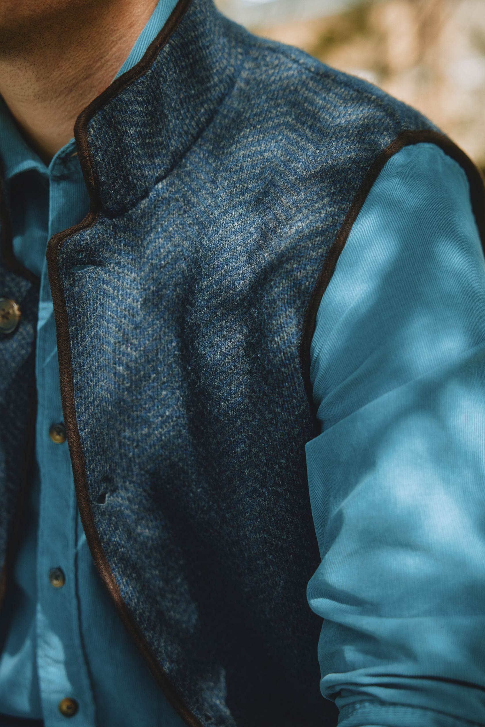 Person wearing a blue shirt and dark gray vest with a blurred natural background