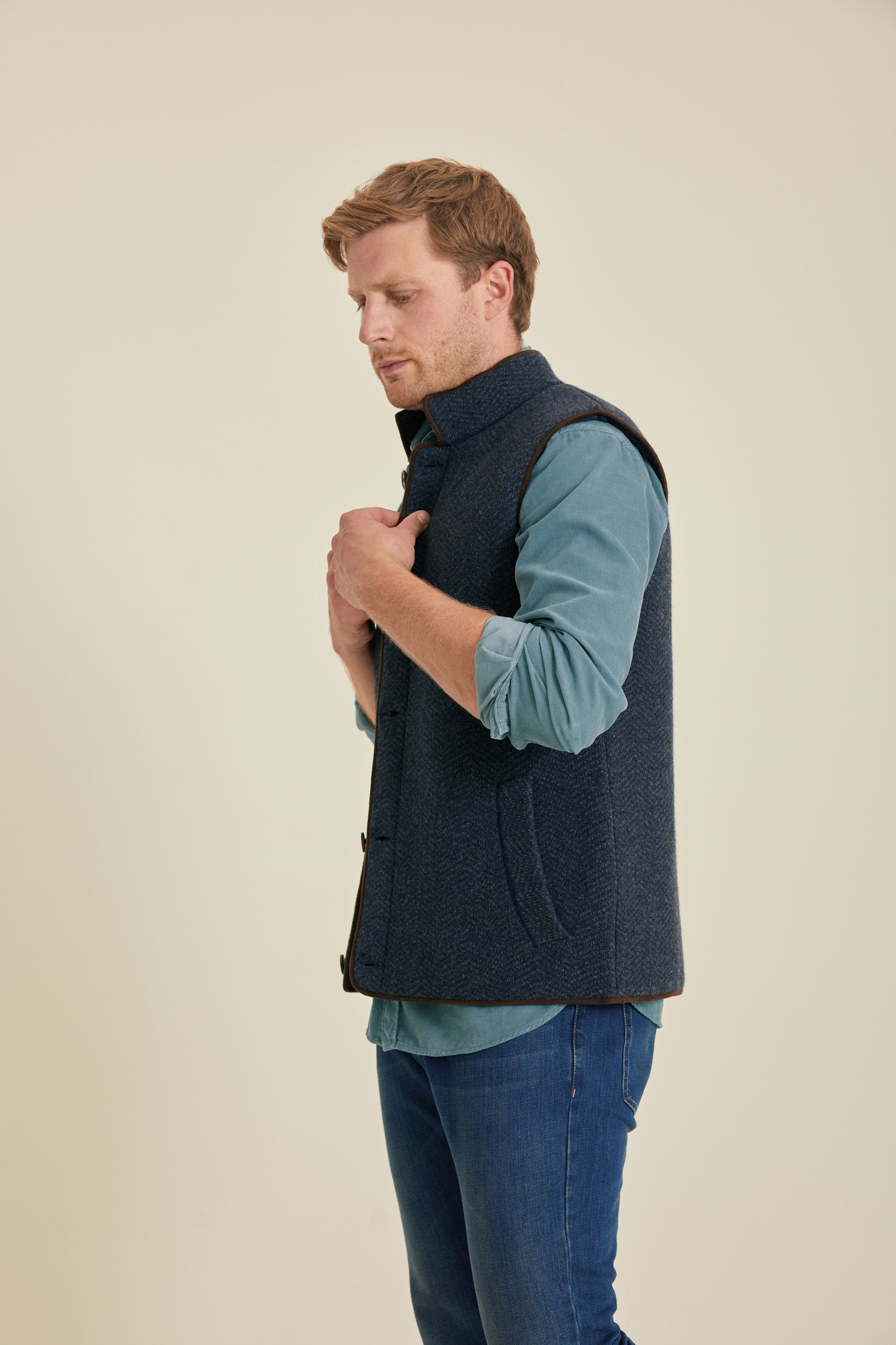 Man wearing a navy blue vest over a light blue shirt on a beige background
