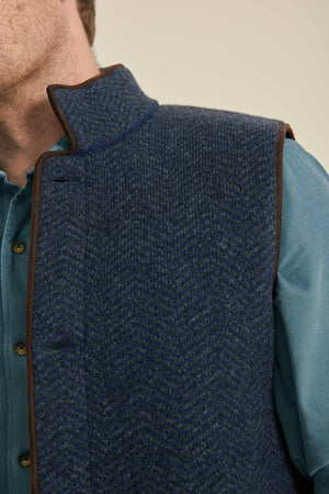 Blue textured vest with brown trim worn over a light blue shirt.
