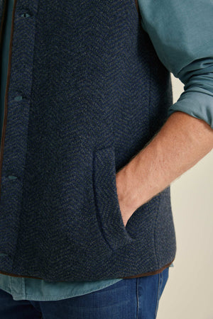 Person wearing a dark blue textured vest over a light blue shirt.
