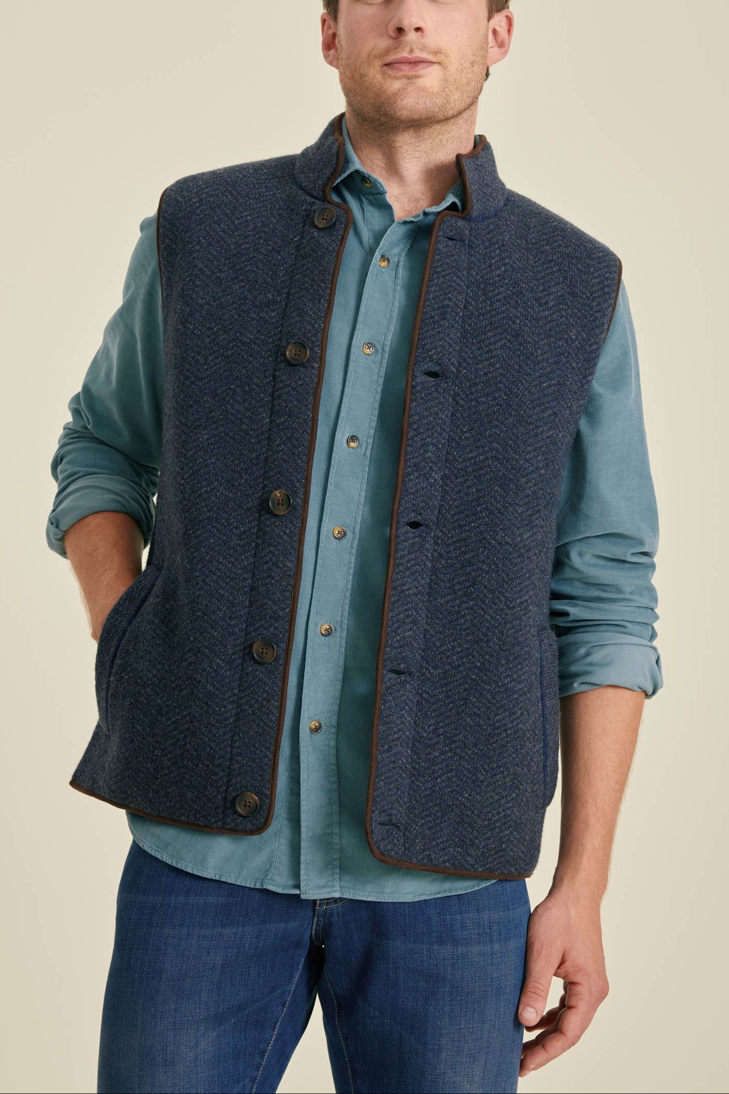 Man wearing a blue vest over a light blue shirt on a beige background