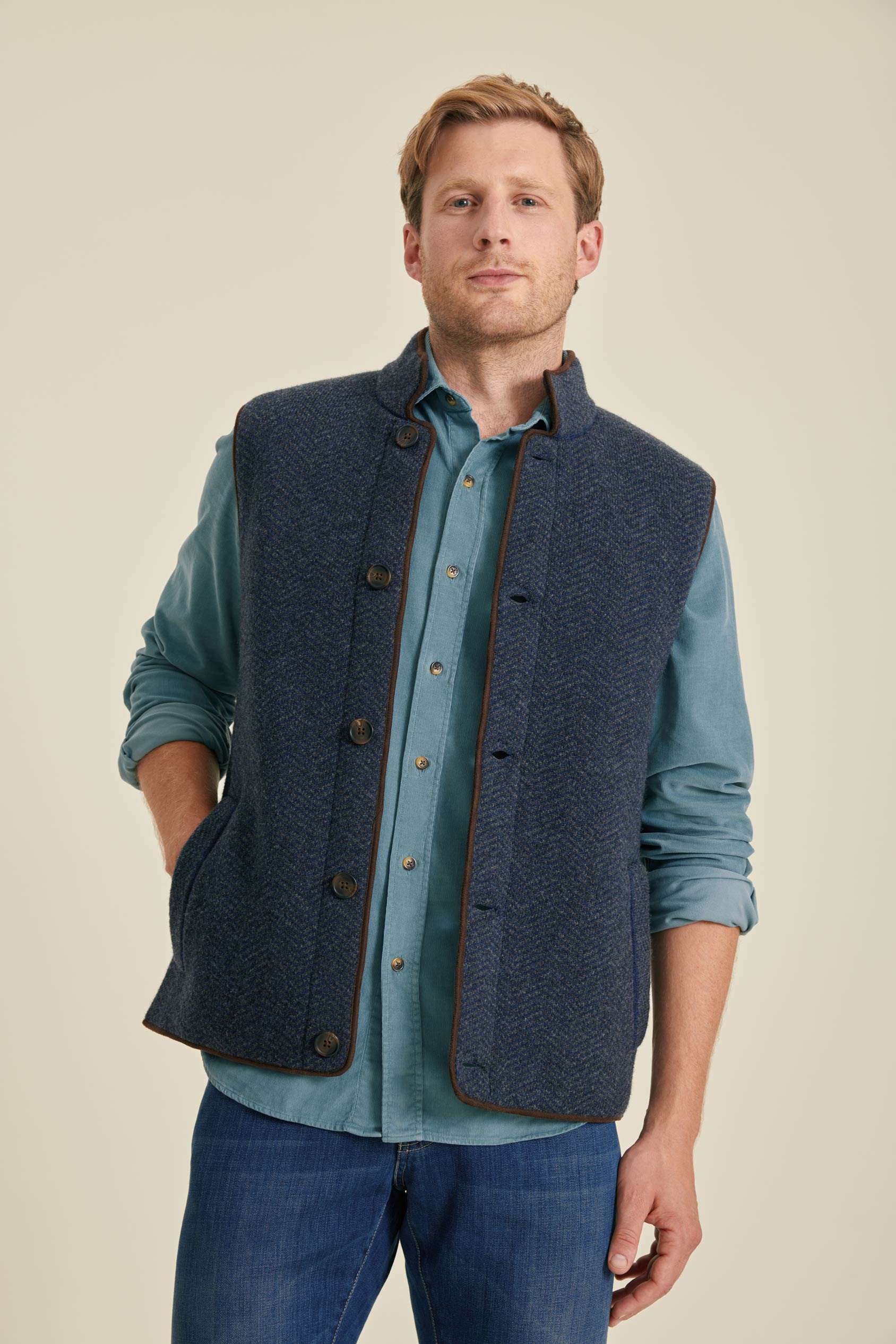 Man wearing a blue vest over a light blue shirt on a beige background