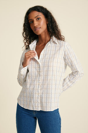 Woman wearing a striped shirt and blue jeans against a beige background