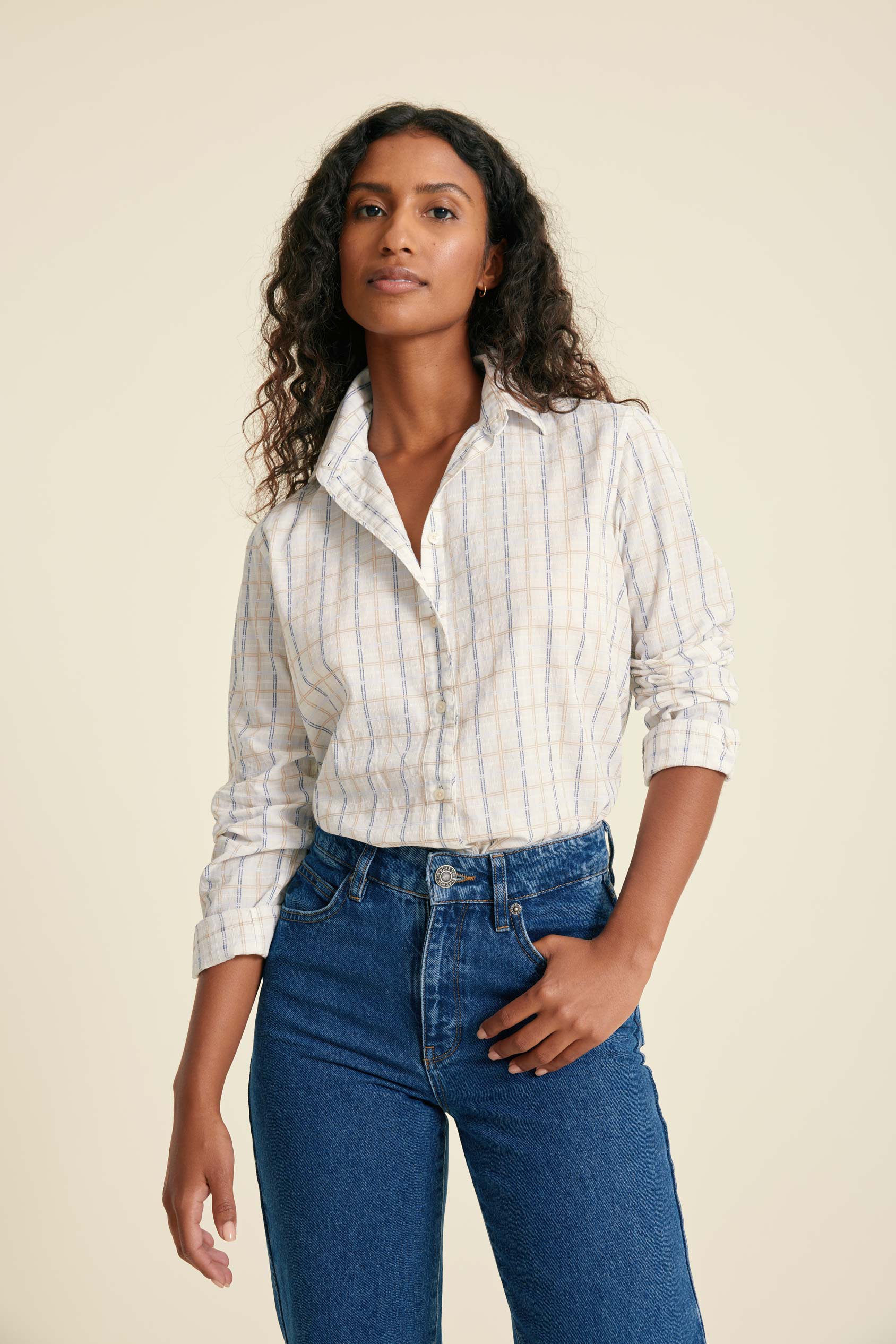 Woman wearing a striped shirt and blue jeans against a beige background