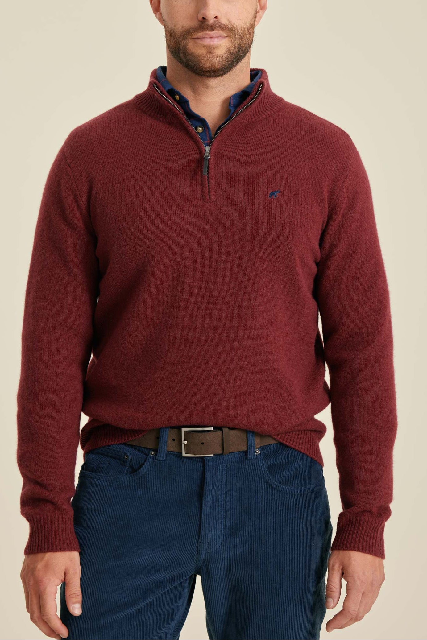 Man wearing a red sweater with a visible brand logo on a beige background