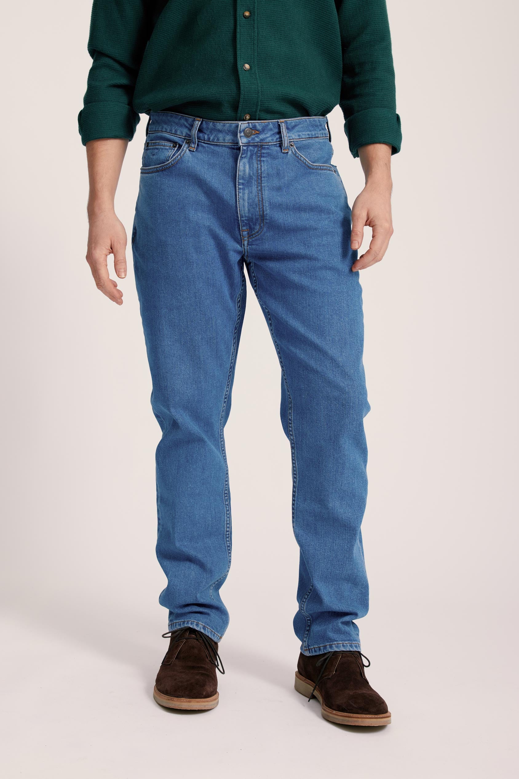 Person wearing blue jeans and a green shirt on a plain background