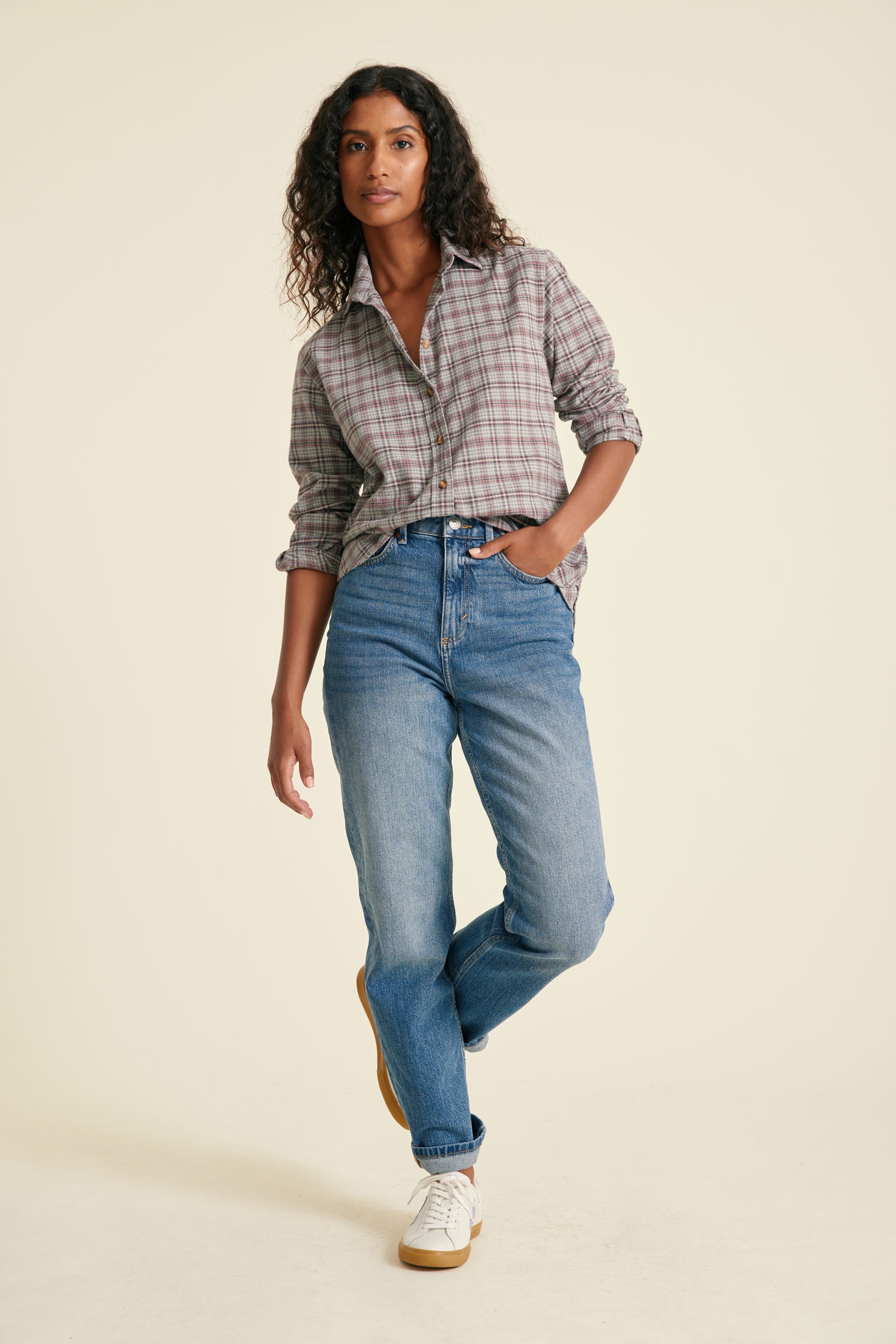 Woman wearing a plaid shirt and blue jeans on a beige background