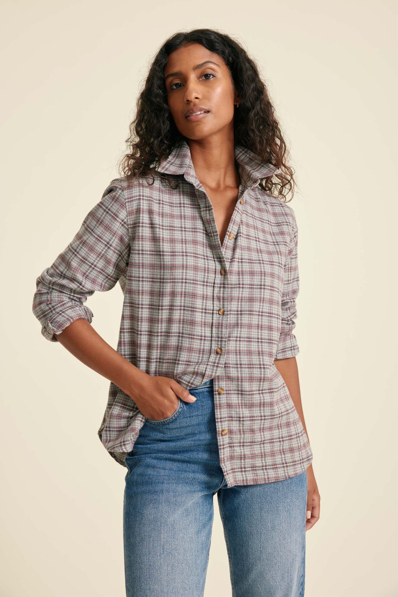 Woman wearing a plaid shirt and jeans against a beige background