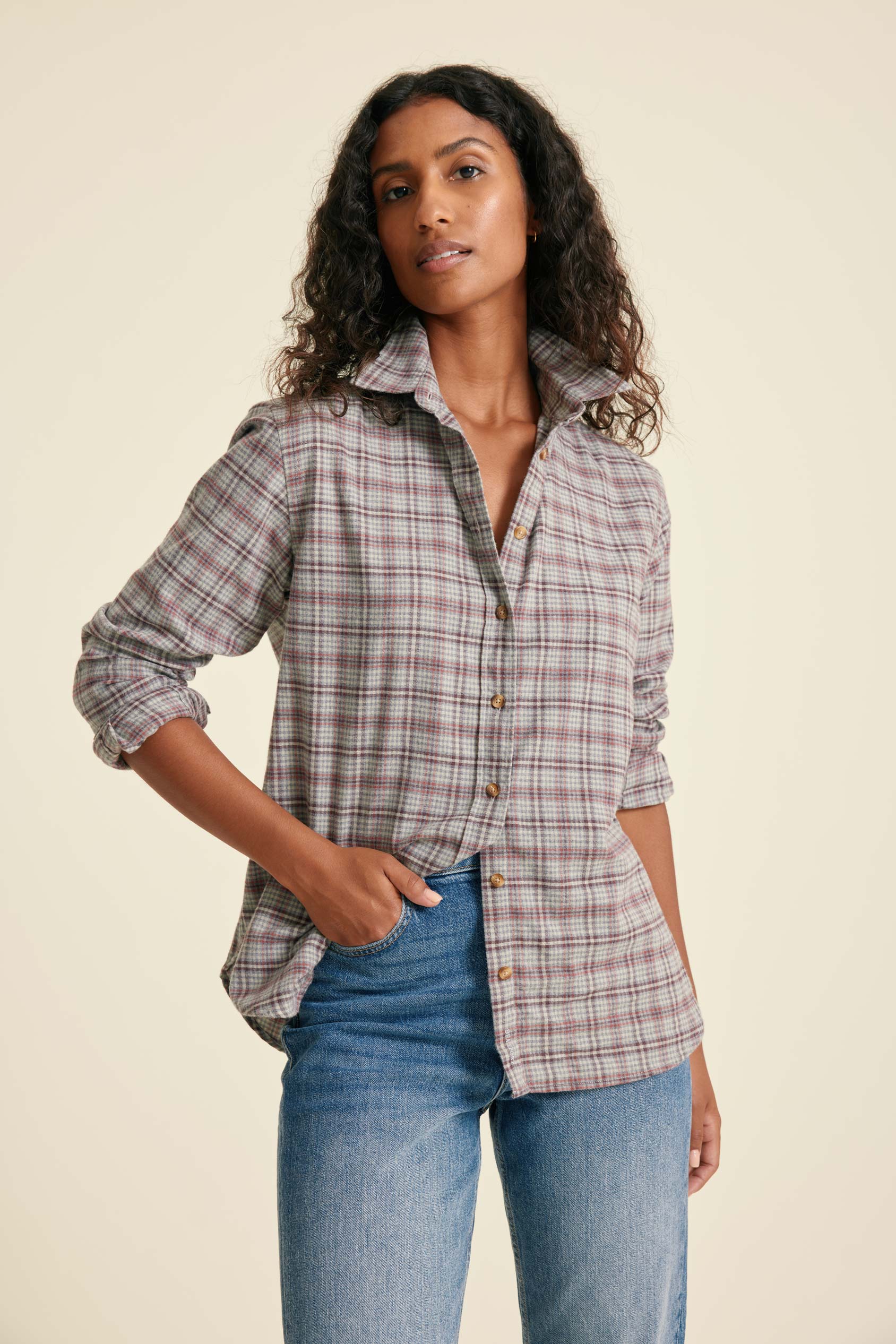 Woman wearing a plaid shirt and jeans against a beige background