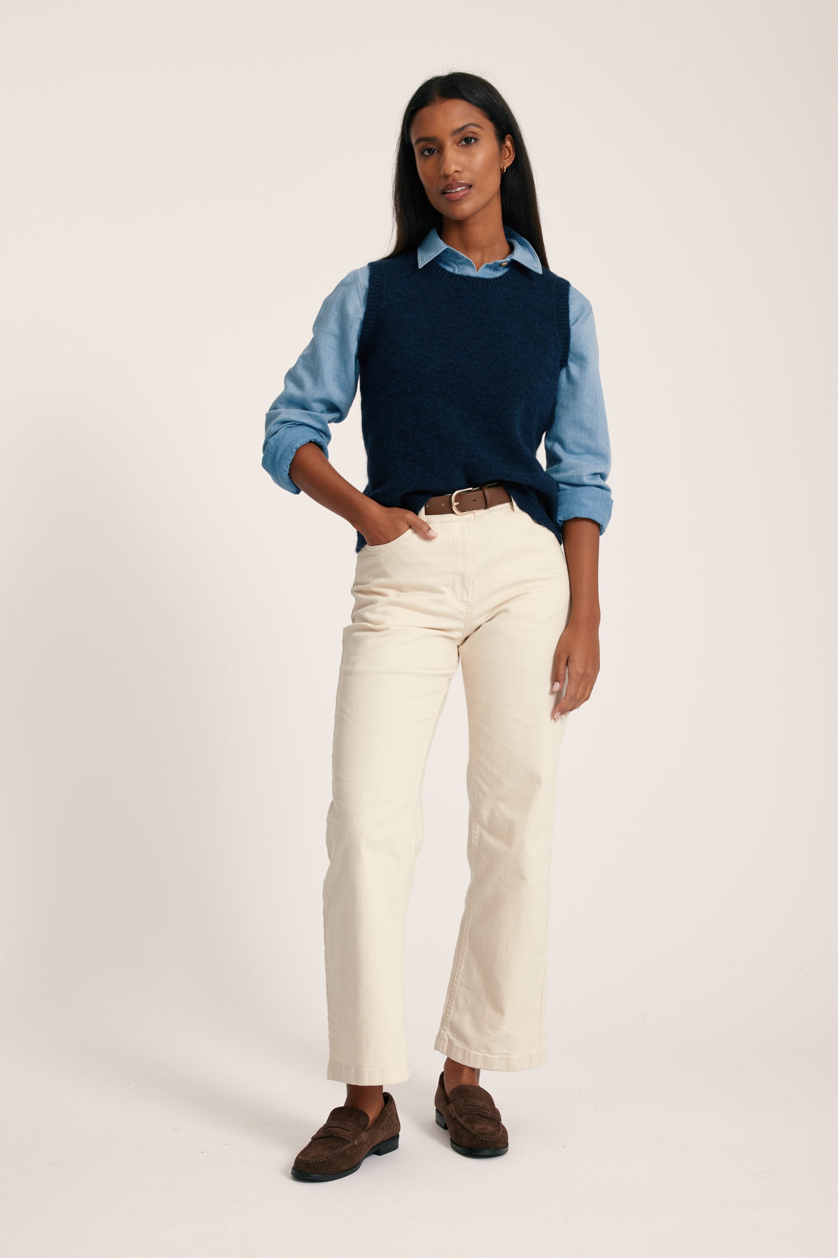 Woman wearing a navy sweater over a light blue shirt with beige pants on a white background