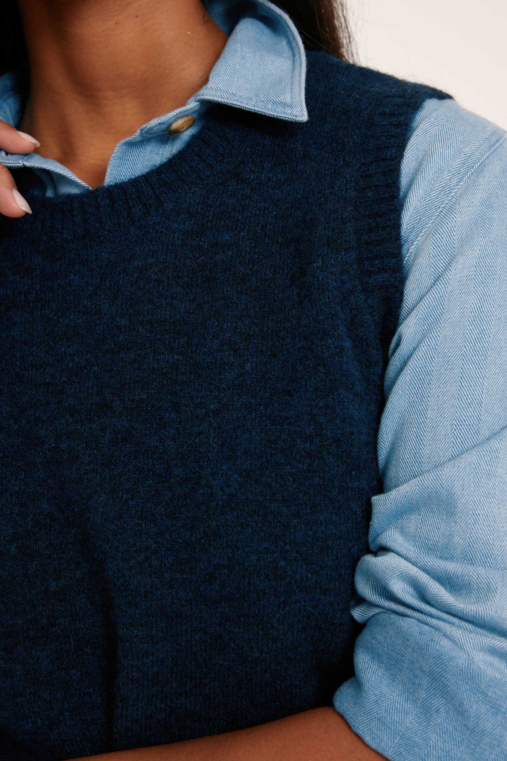Person wearing a dark blue knitted vest over a light blue shirt
