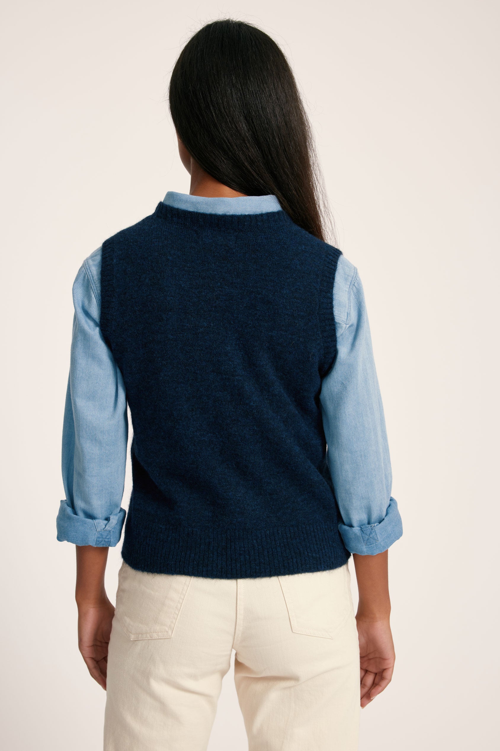 Person wearing a navy sweater vest over a blue shirt with beige pants on a light background