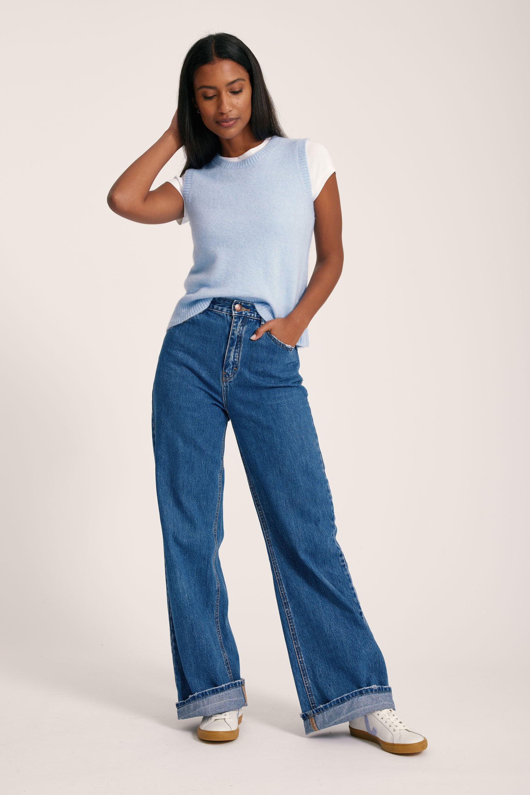 Woman wearing a light blue sleeveless top and blue jeans on a white background