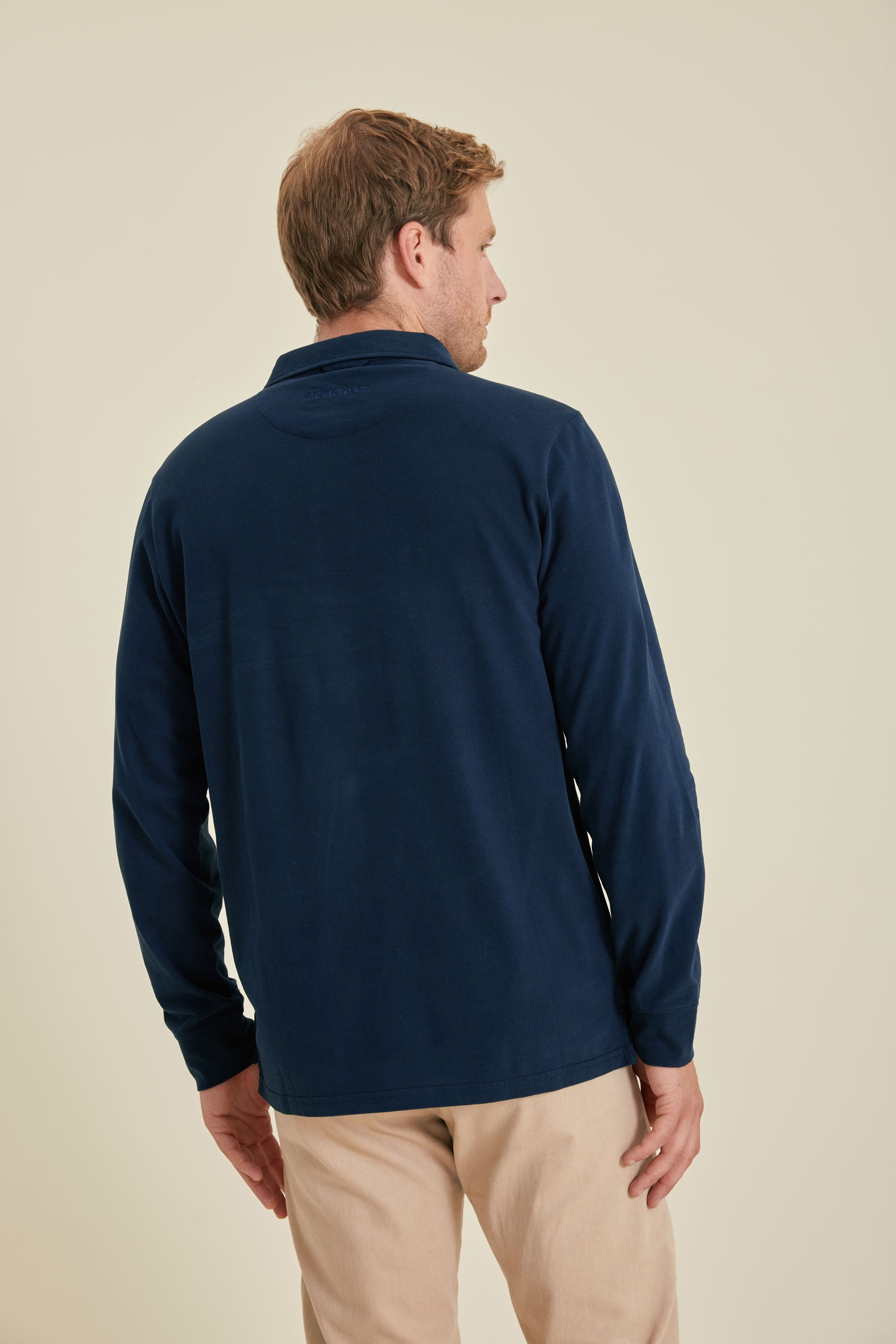 Man wearing a navy long-sleeve shirt and beige pants on a beige background