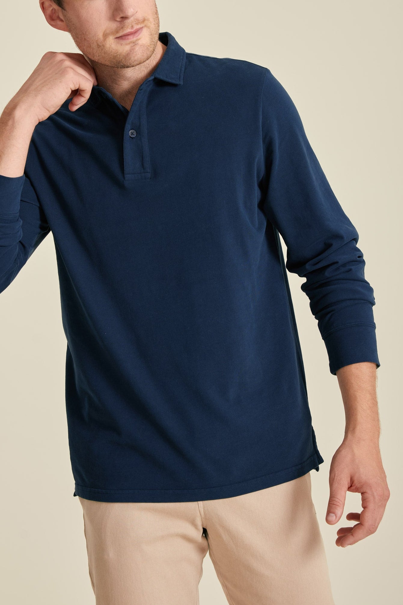 Man wearing a navy long-sleeve polo shirt against a beige background