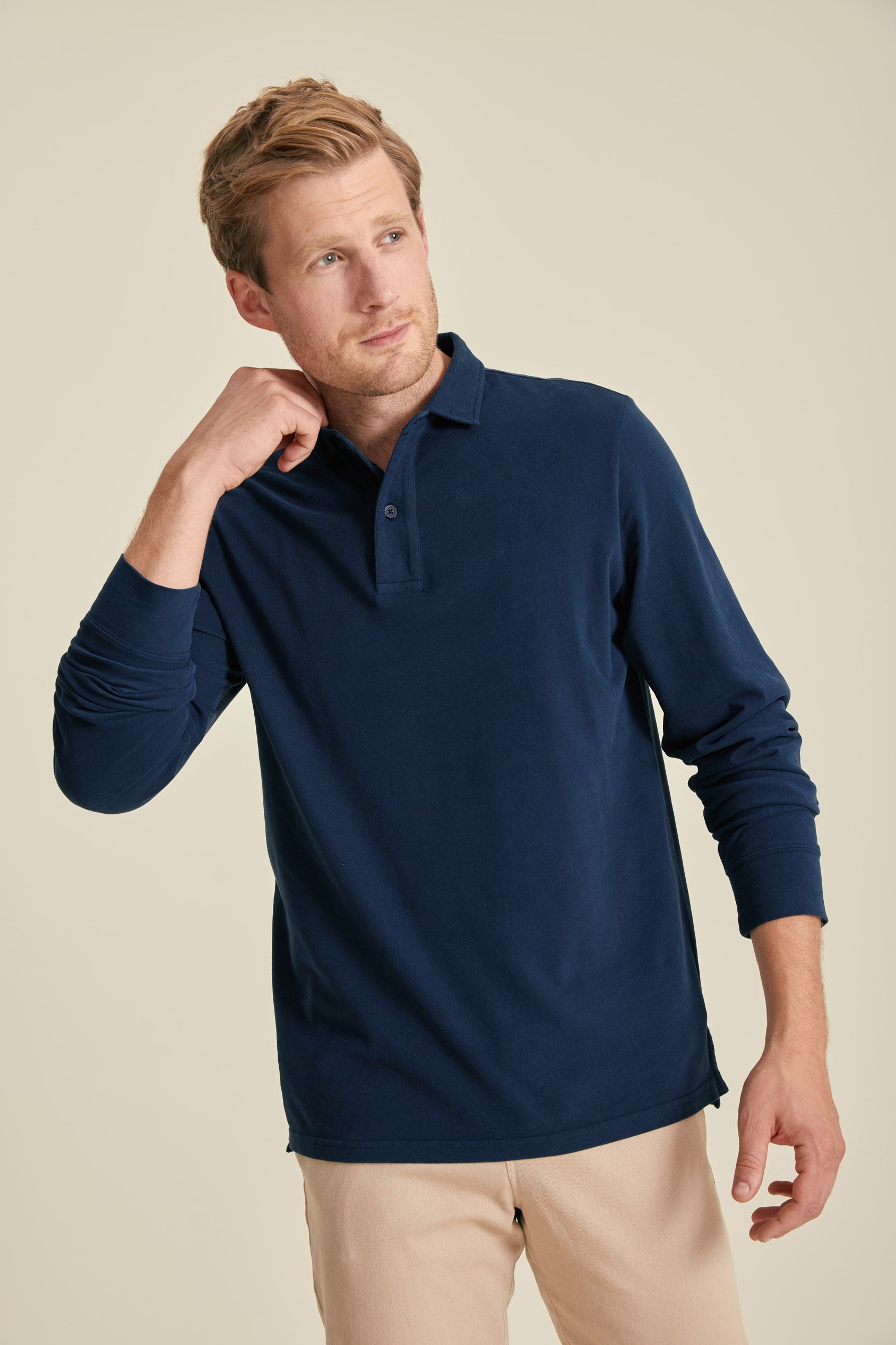 Man wearing a navy long-sleeve polo shirt against a beige background