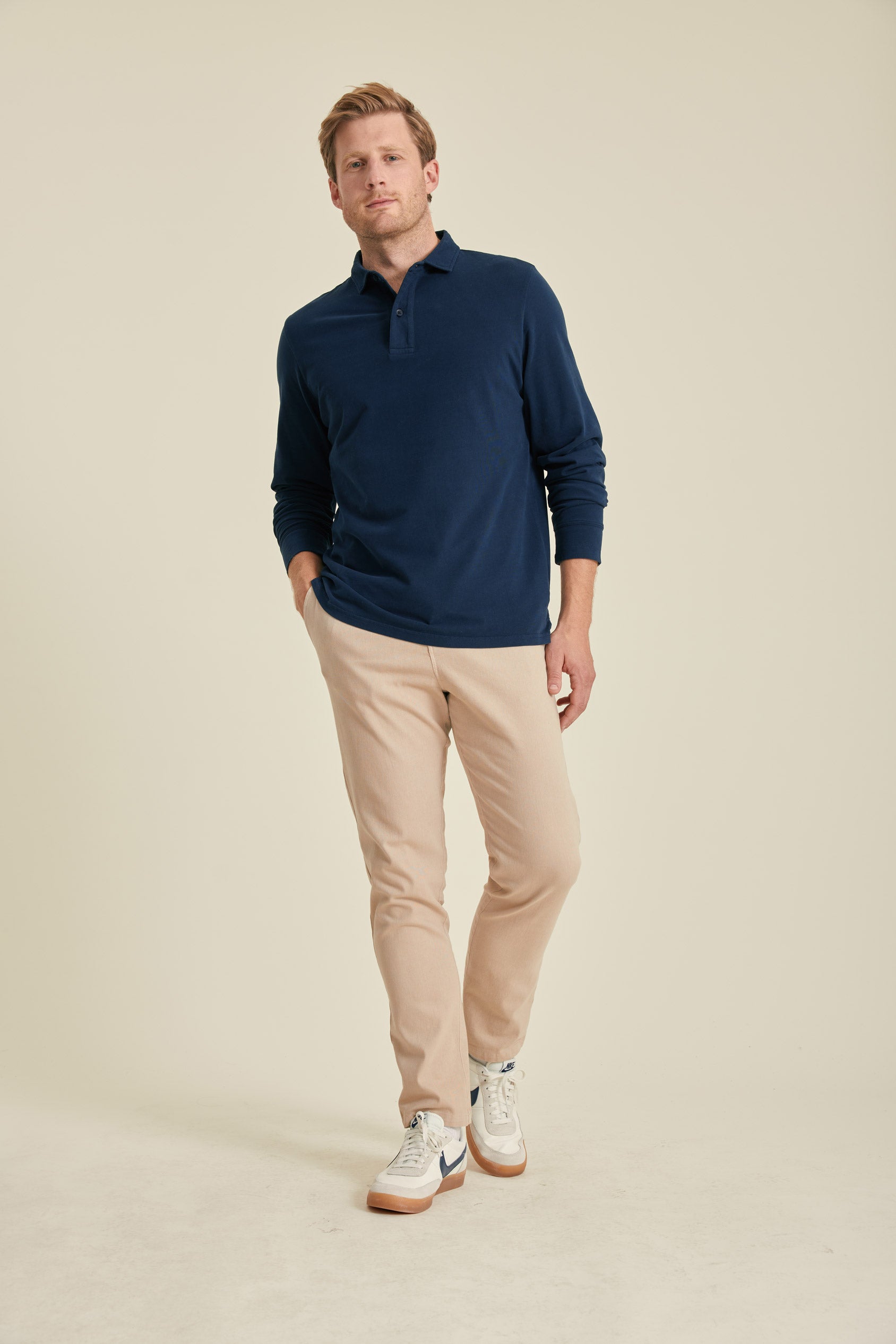 Man wearing a navy polo shirt and beige pants on a beige background