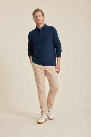 Man wearing a navy polo shirt and beige pants on a beige background