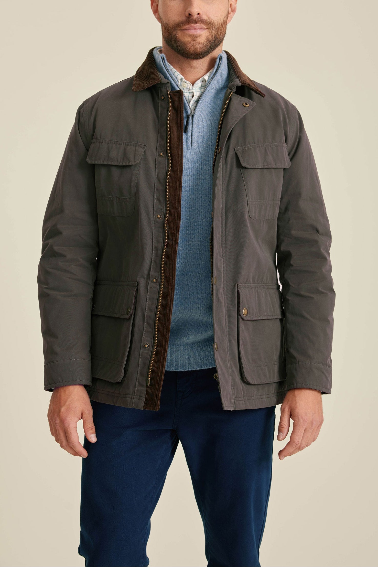 Man wearing a dark brown jacket over a blue shirt and pants on a beige background