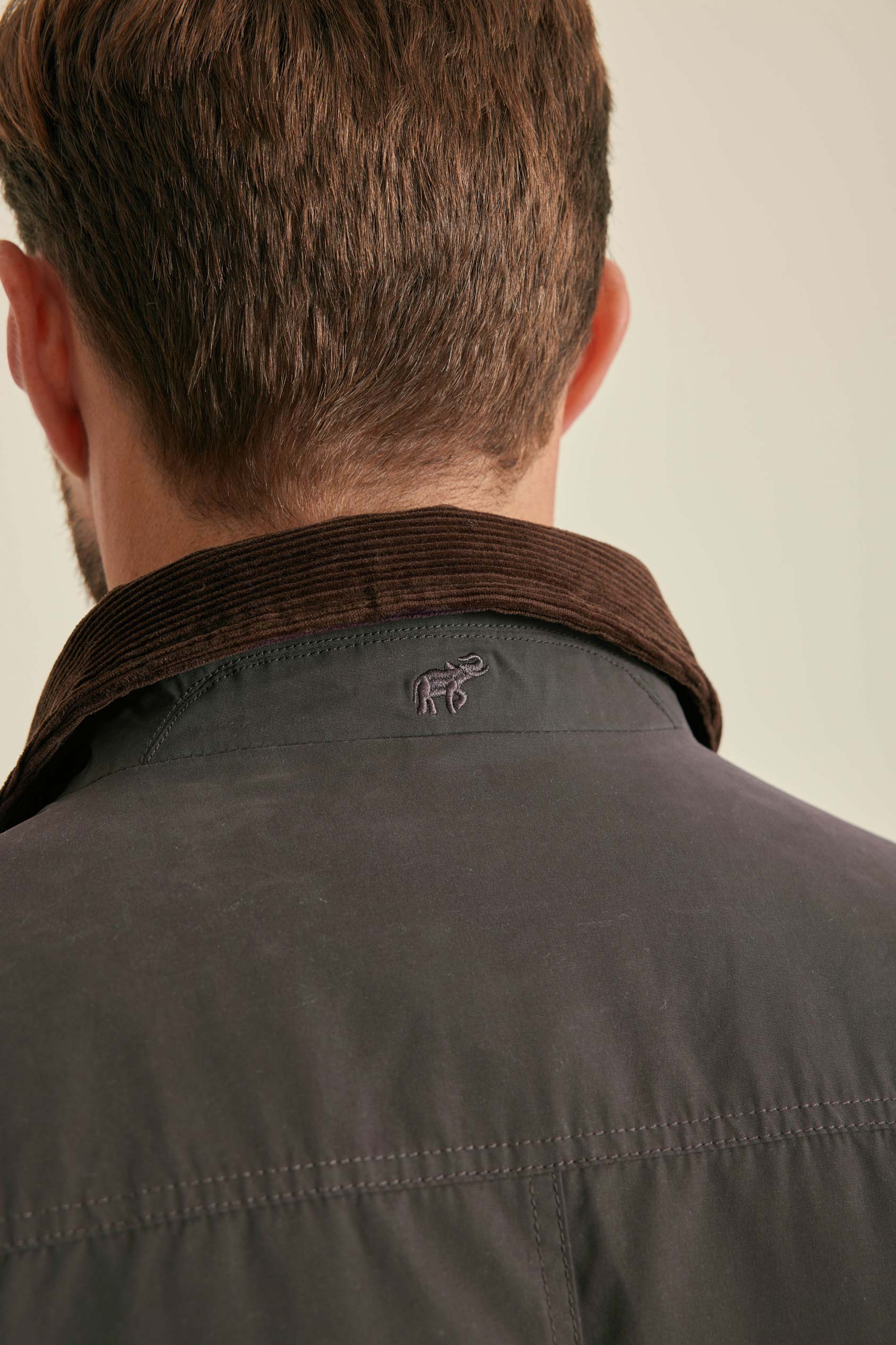 Man wearing a dark jacket with a visible brand logo on a plain background