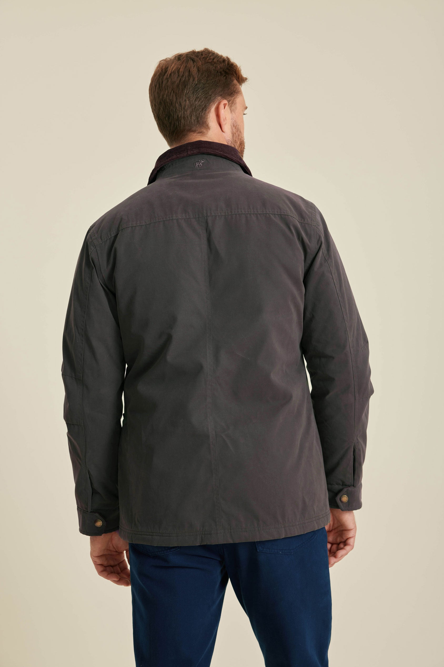 Man wearing a dark jacket and blue pants on a beige background