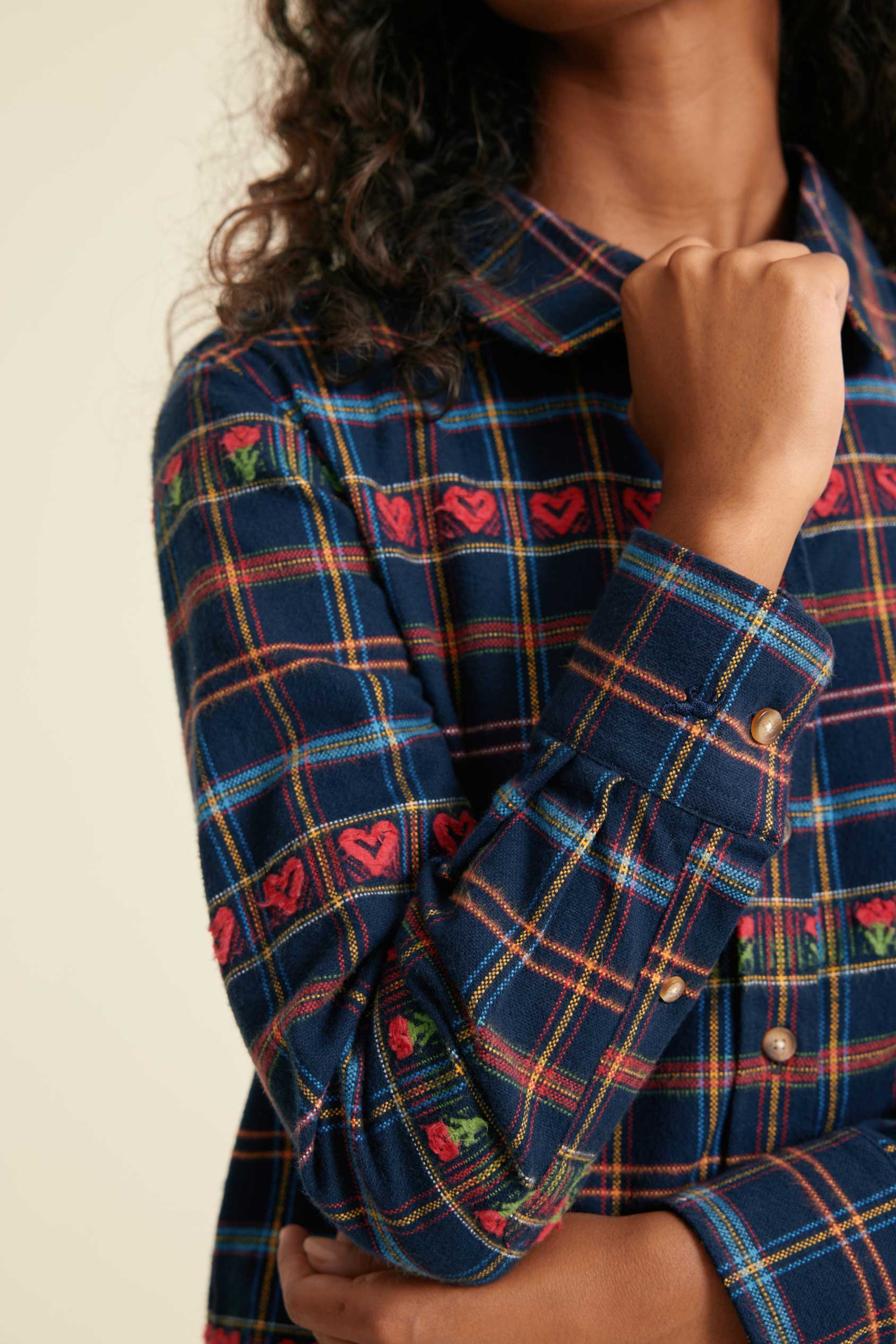 Close-up of a person wearing a blue plaid shirt with red heart patterns on a beige background