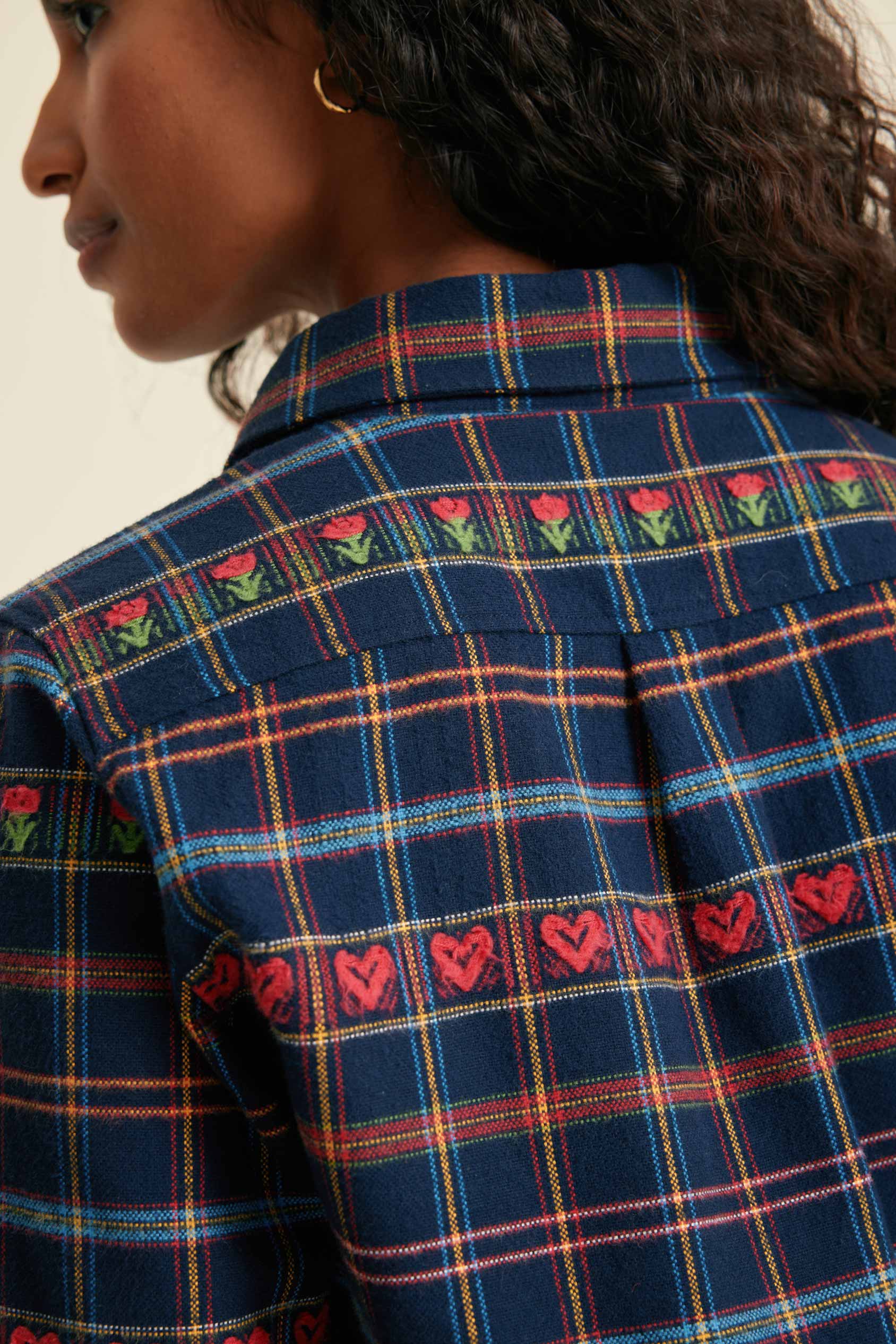 Close-up of a blue plaid shirt with embroidered designs on a neutral background