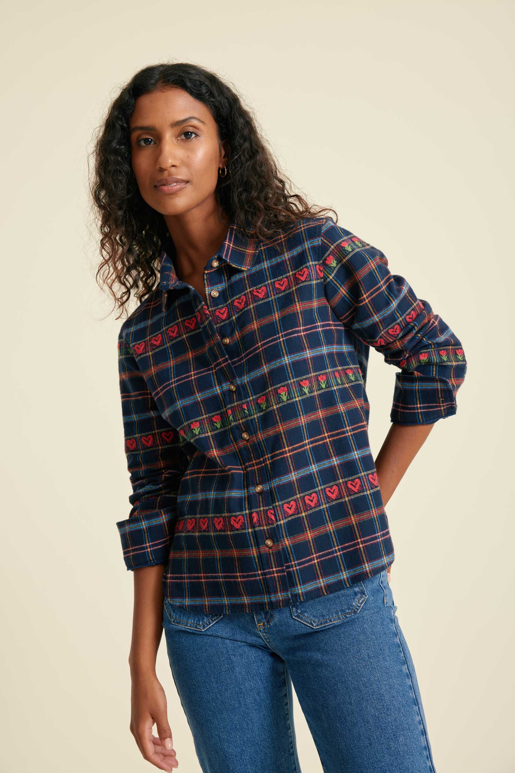Woman wearing a plaid shirt with heart patterns and blue jeans on a beige background